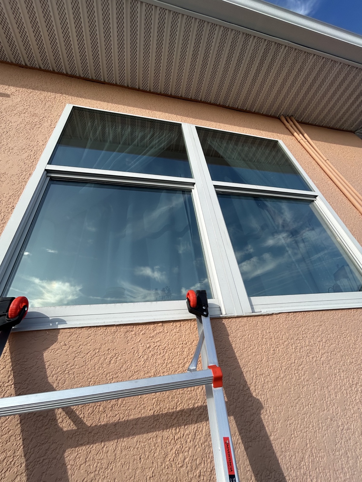 Clean residential windows reflecting the sky above a safely positioned ladder